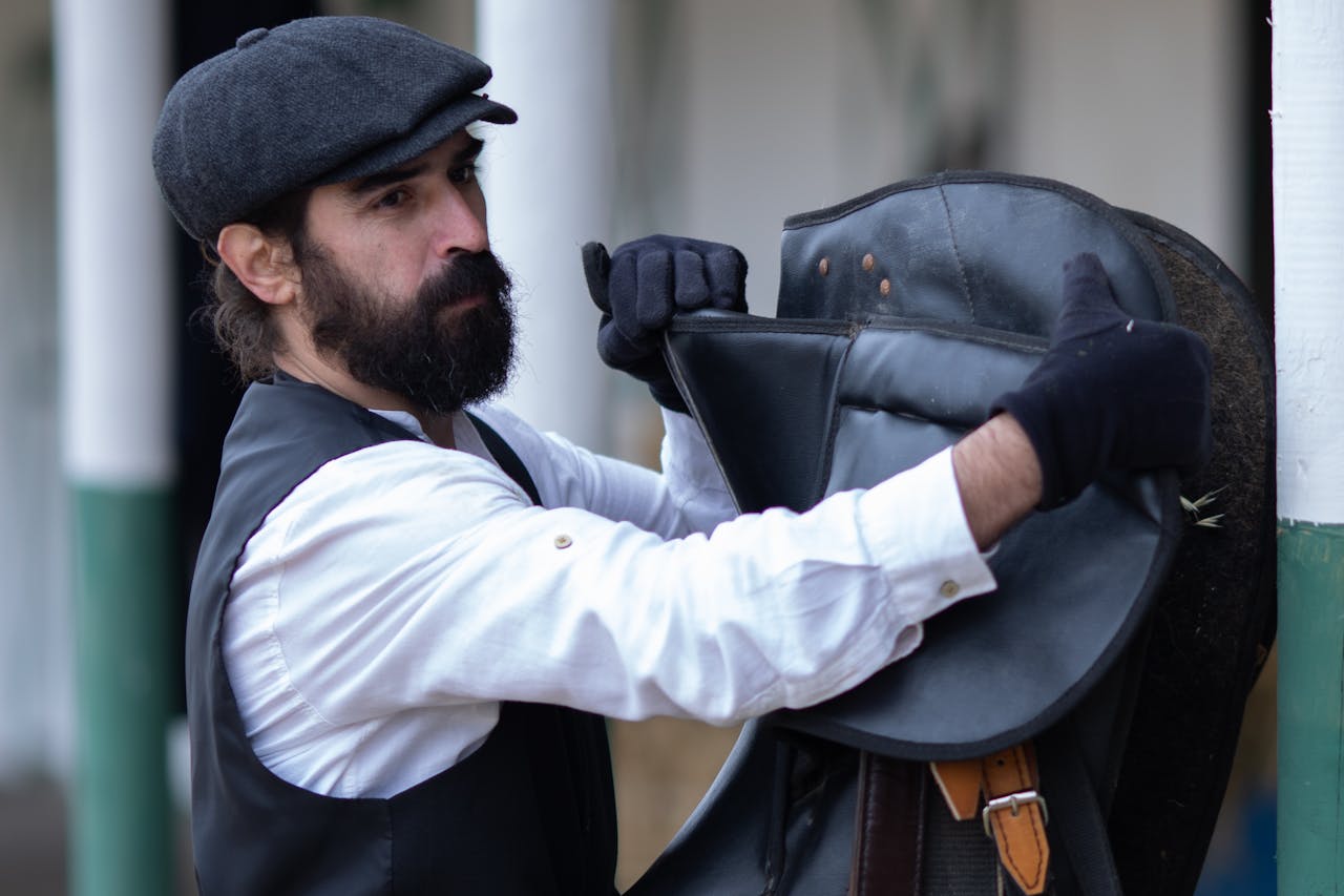 A bearded man in a flat cap organizing horse saddle outdoors in Baku, Azerbaijan.